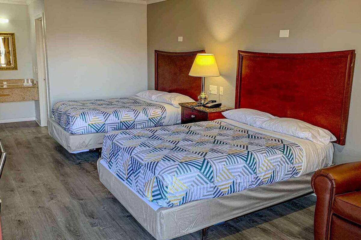 A hotel room with two beds, a desk, a chair, a lamp, and a mirror.