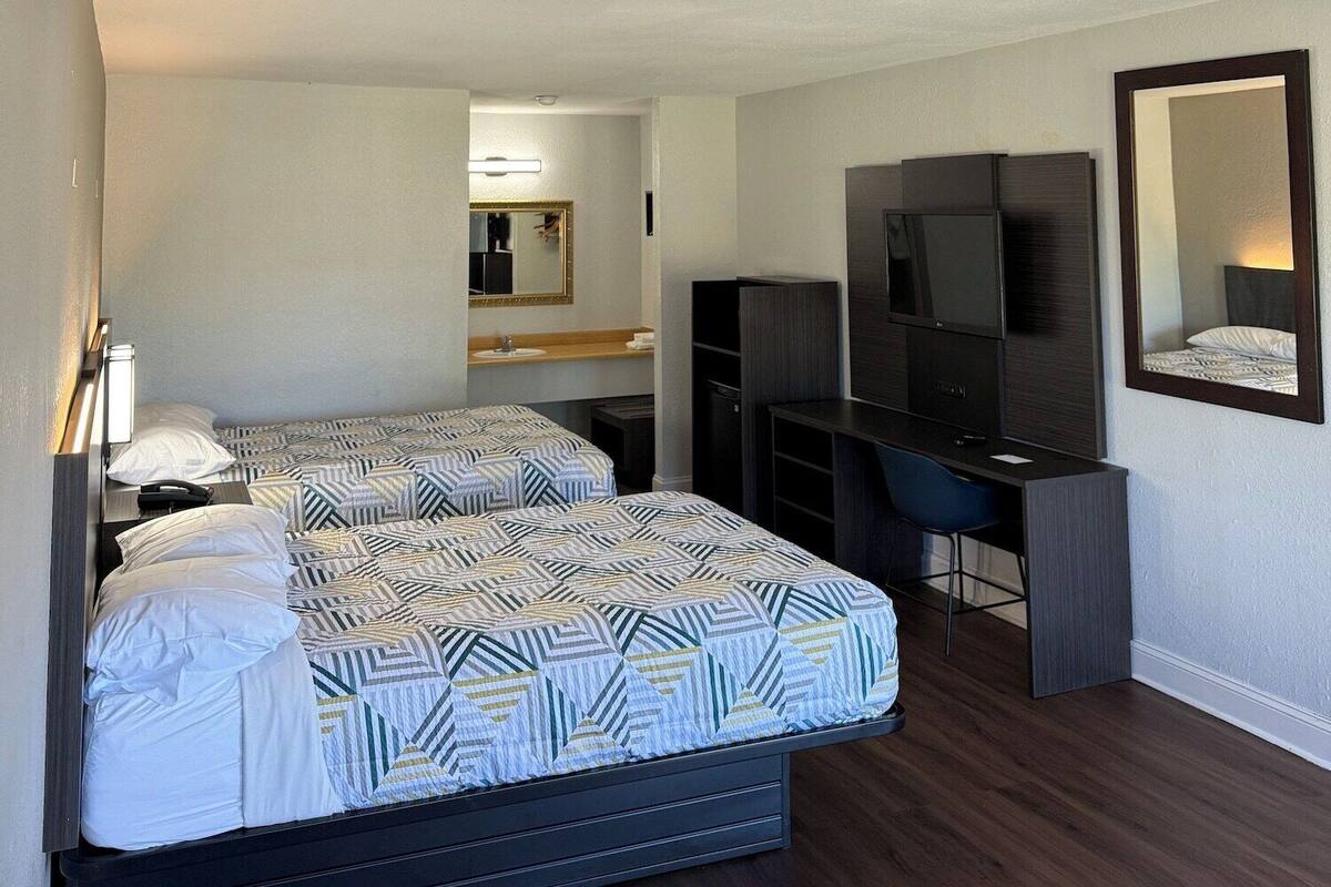 A hotel room with two beds, a desk, a TV, and a mirror.