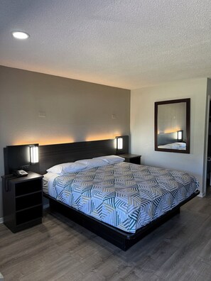 Un cuarto de hotel ordenado con una cama, mesitas de noche, un teléfono y un espejo.