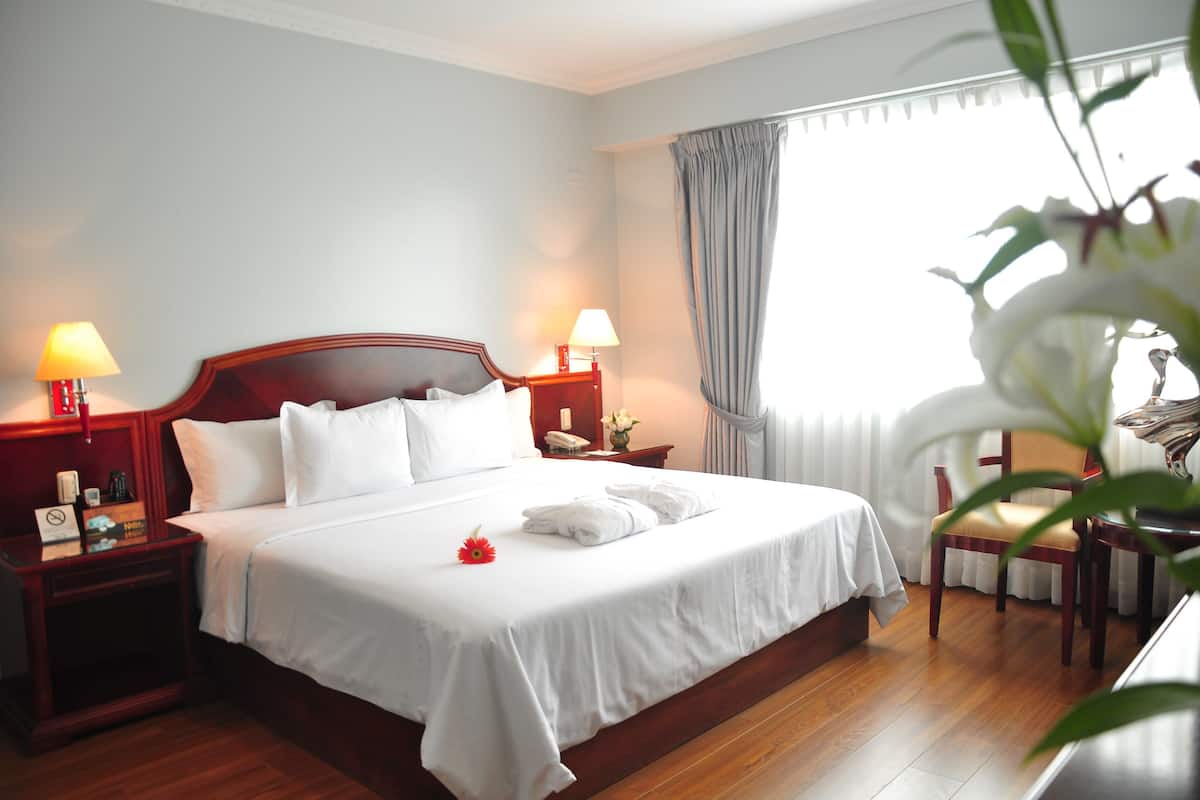 A hotel room with a large bed, two bedside tables with lamps, a chair, and a window with curtains.