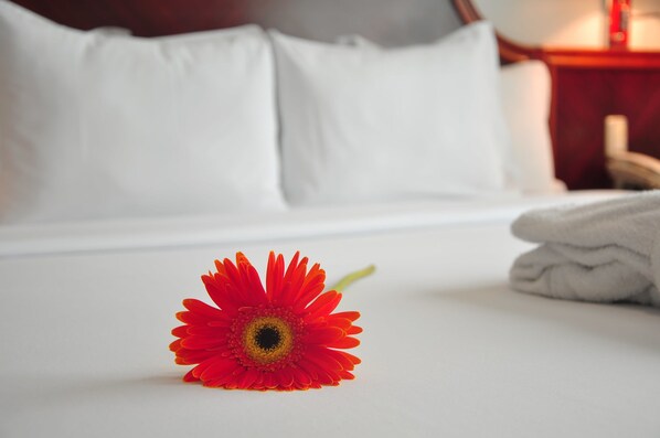 A neatly made bed with white linens, a single red flower on the bed, and a folded towel to the right. - Kingdom Hotel (Lima)