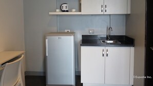 Cocina compacta con refrigerador, lavamanos y armarios blancos.