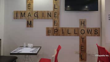A room with a wooden wall puzzle, a flat-screen TV, a table with a drawing, and red chairs.