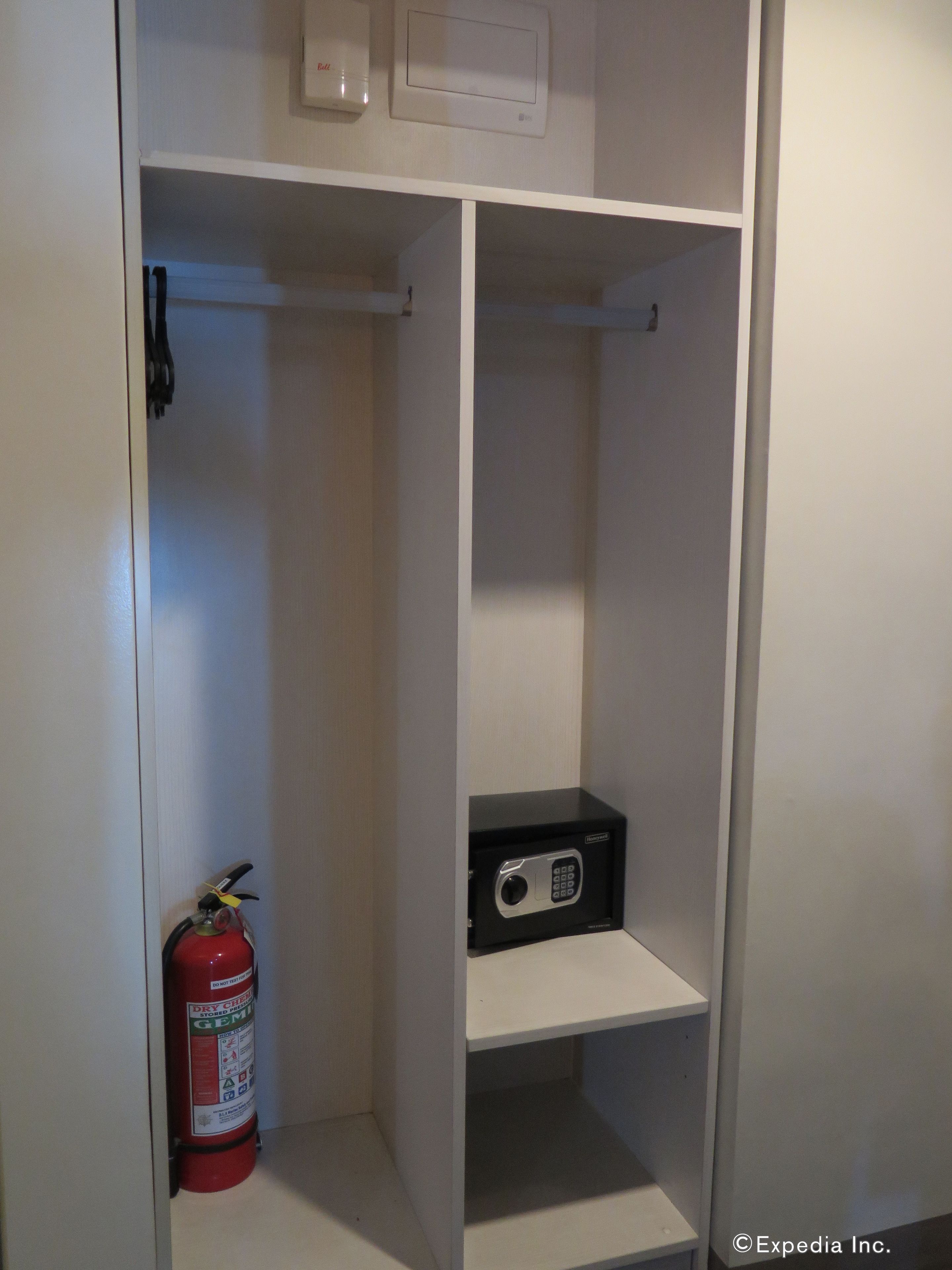A closet with a fire extinguisher and a black electronic device on a shelf.