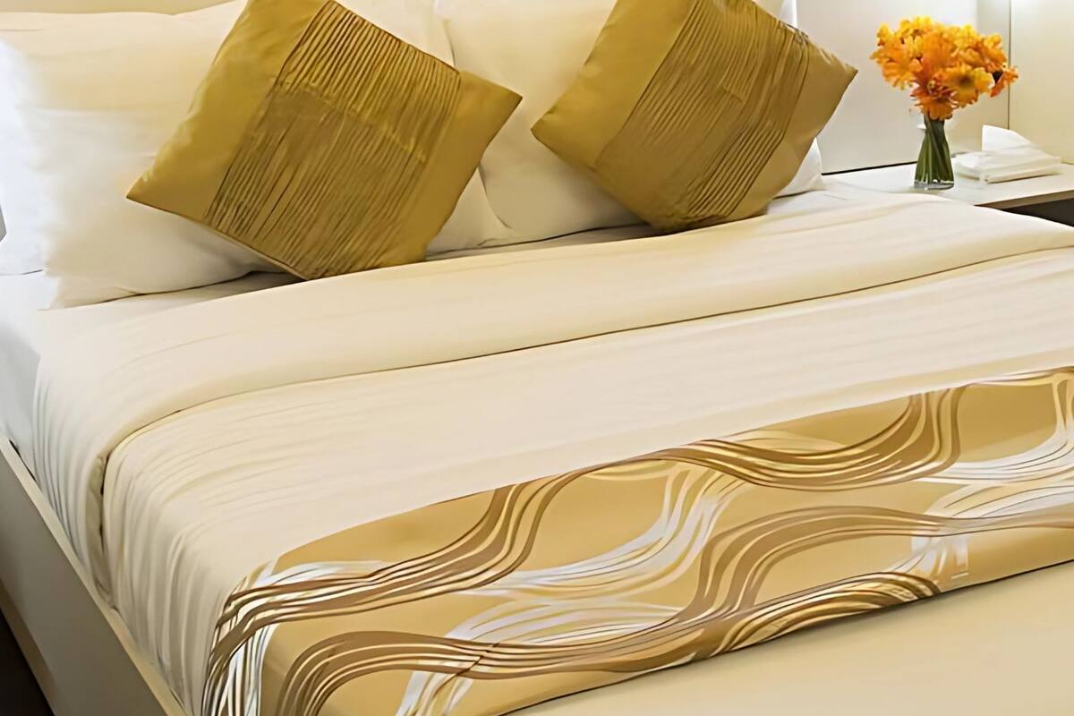 A hotel room with a large bed, two gold pillows, white bedding, and a vase of orange flowers.