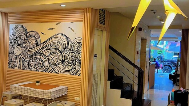 Un interior moderno con zona de comedor que incluye mesas y sillas, una escalera y una pared con un mural en blanco y negro.