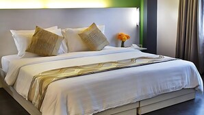Una cama bien hecha con sábanas blancas y almohadas decorativas, una mesita de noche con un florero y una pared de acento verde.