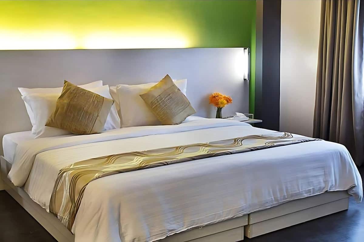 A neatly made bed with white linens and decorative pillows, a bedside table with a vase of flowers, and a green accent wall.