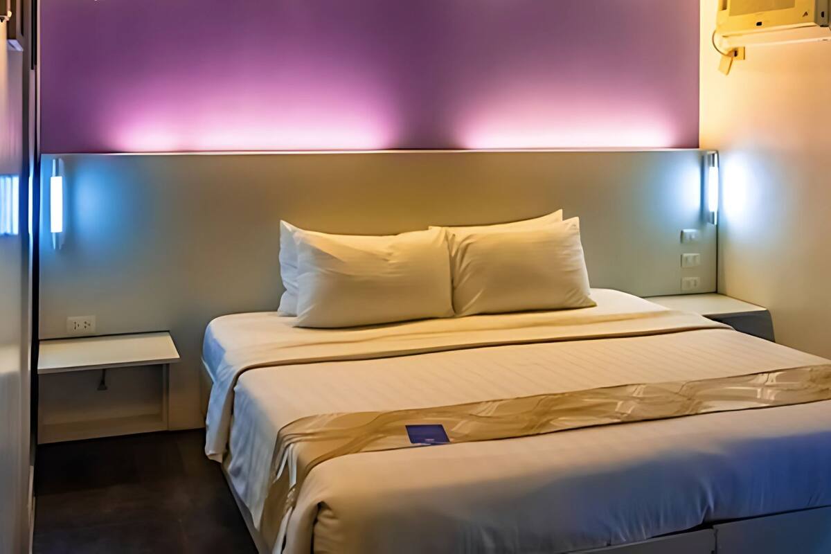 A hotel room with a bed, nightstands, and a headboard with ambient lighting.