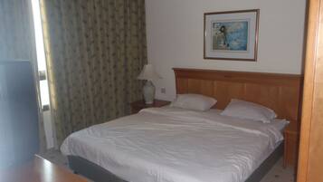Una habitación de hotel con una cama, una mesita de noche, una lámpara, un cuadro en la pared y una ventana con cortinas.