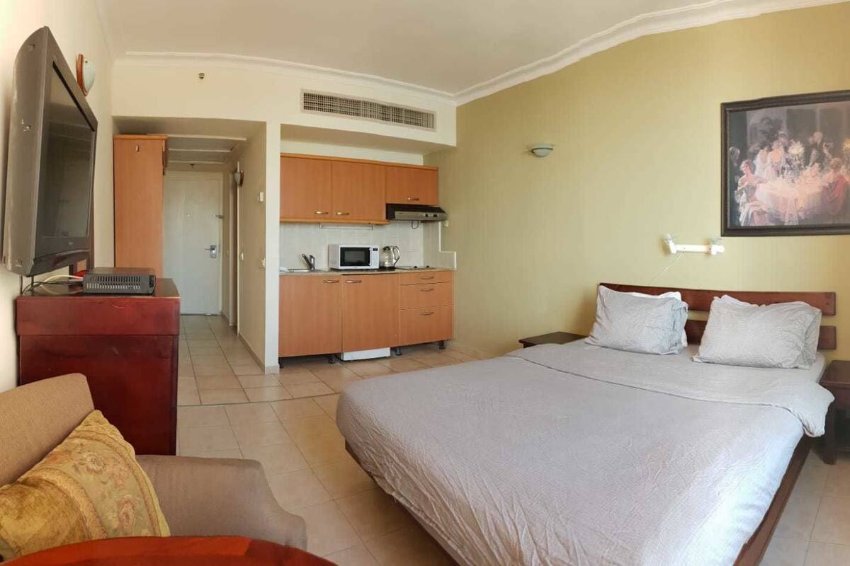 Une chambre d’hôtel avec un grand lit, un bureau avec un ordinateur, une kitchenette et un tableau au mur.