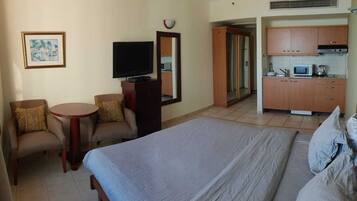 Habitación de hotel con una cama, dos sillones, una mesita, televisor, espejo y una kitchenette con microondas.