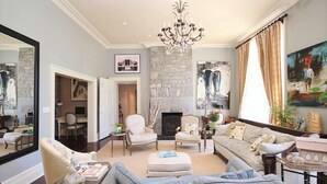 A spacious living room with a fireplace, comfortable seating, and a large mirror. - All Suites Whitney Manor (Kingston)