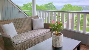A wicker sofa with patterned cushions on a balcony with a white railing, overlooking a green landscape and water. - All Suites Whitney Manor (Kingston)