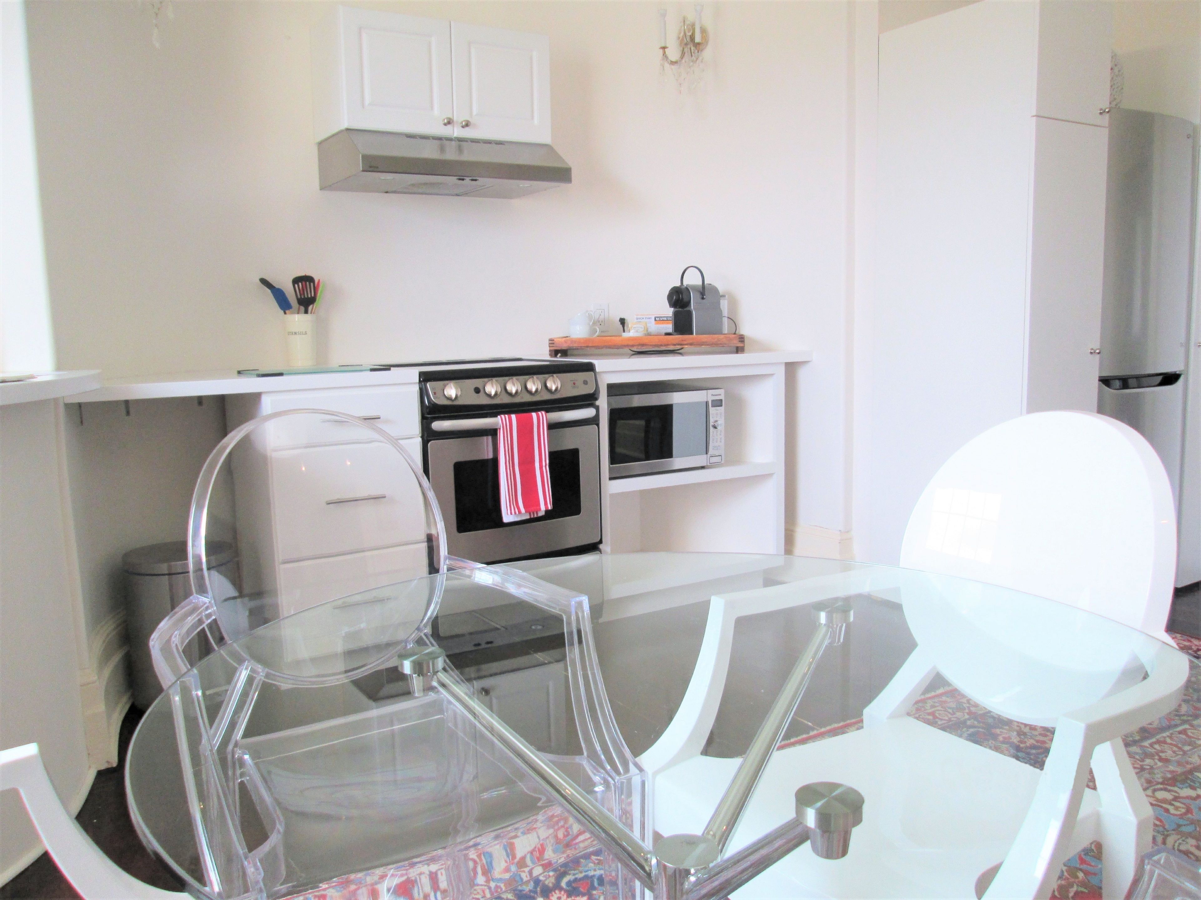 A modern kitchen with white cabinetry, a stainless steel oven, a microwave, and a glass dining table with chairs.