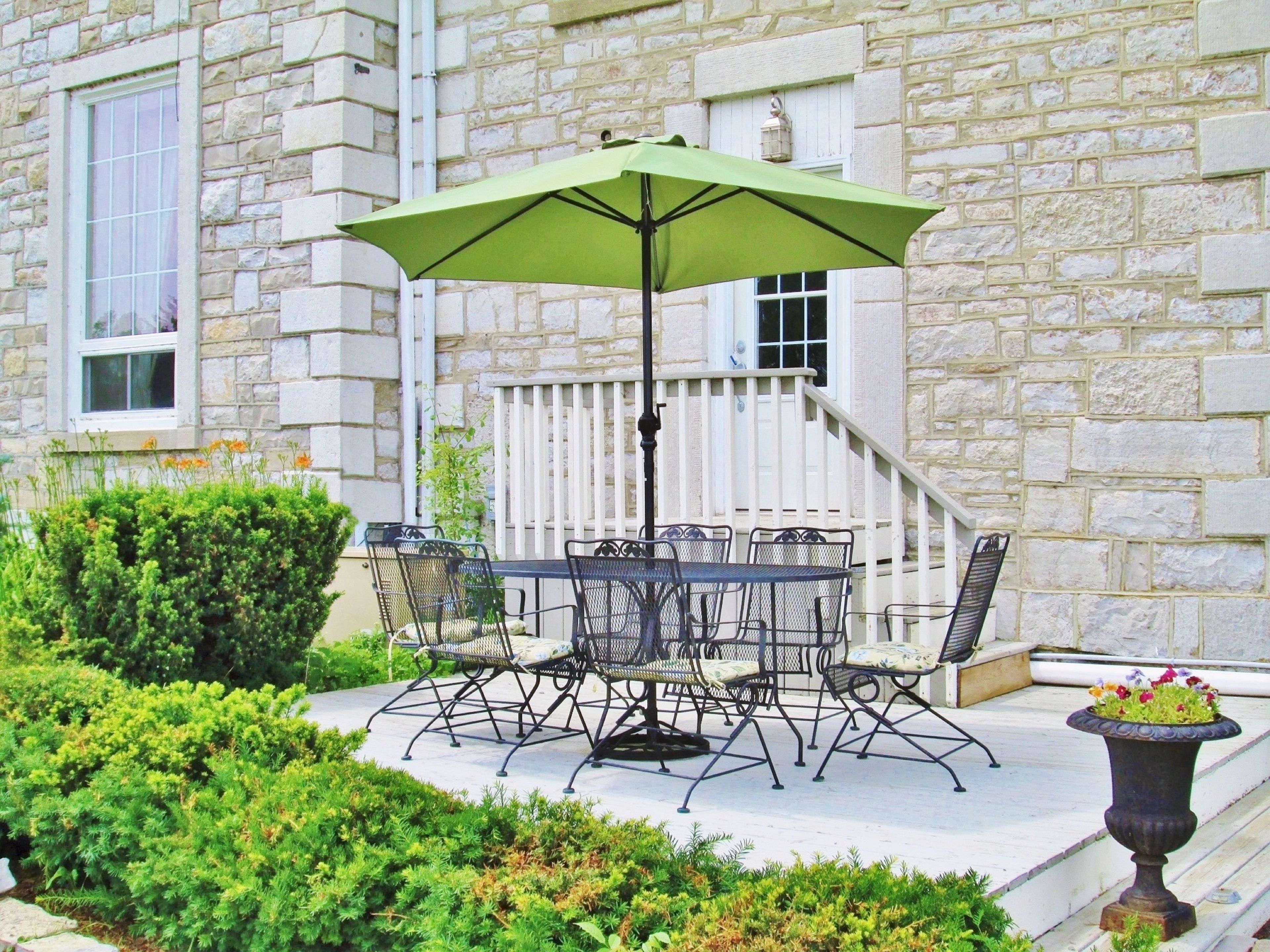 A stone building with a patio featuring a table and chairs, a green umbrella, and a flower pot.