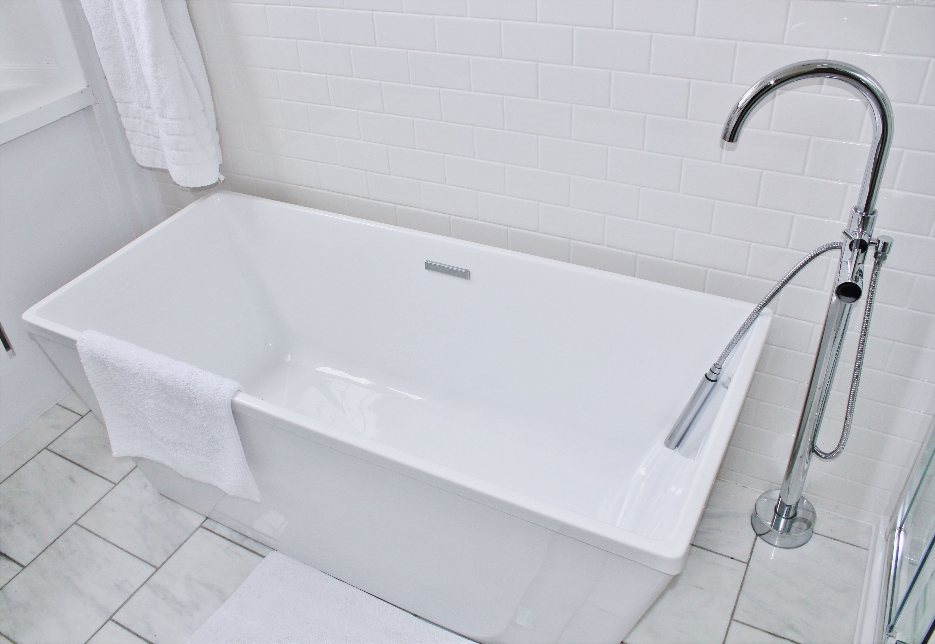 A modern bathroom with a white bathtub, a handheld showerhead, and a white towel hanging on the wall.