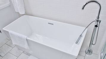 A modern bathroom with a white bathtub, a handheld showerhead, and a white towel hanging on the wall.