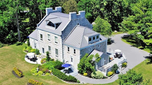 A large, two-story stone house with a wrap-around porch and a landscaped garden. - All Suites Whitney Manor (Kingston)