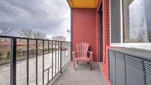 Ein Balkon mit roter Backsteinmauer, einem Fenster mit dekorativem Rollo und einem rosa Stuhl.