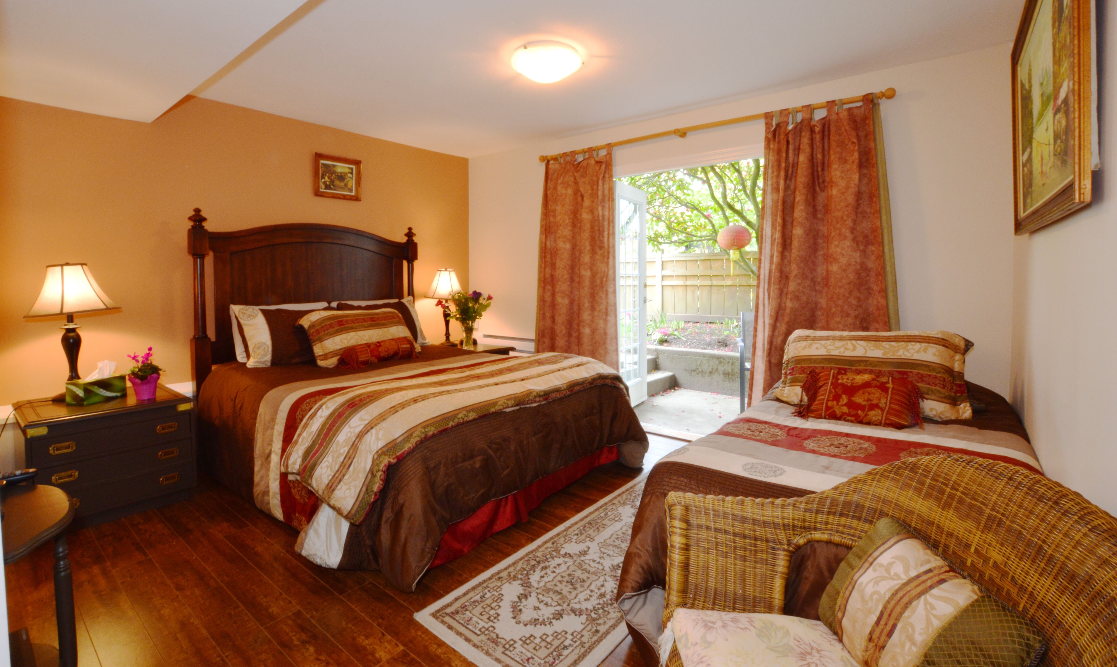 Quarto com cama de madeira, mesa de cabeceira, abajur e vista para o exterior.
