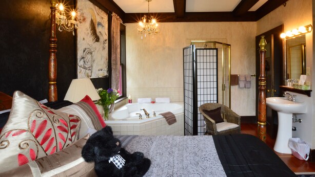 Un dormitorio con cama, sillón, un ventanal grande y un baño con bañera y lavamanos.