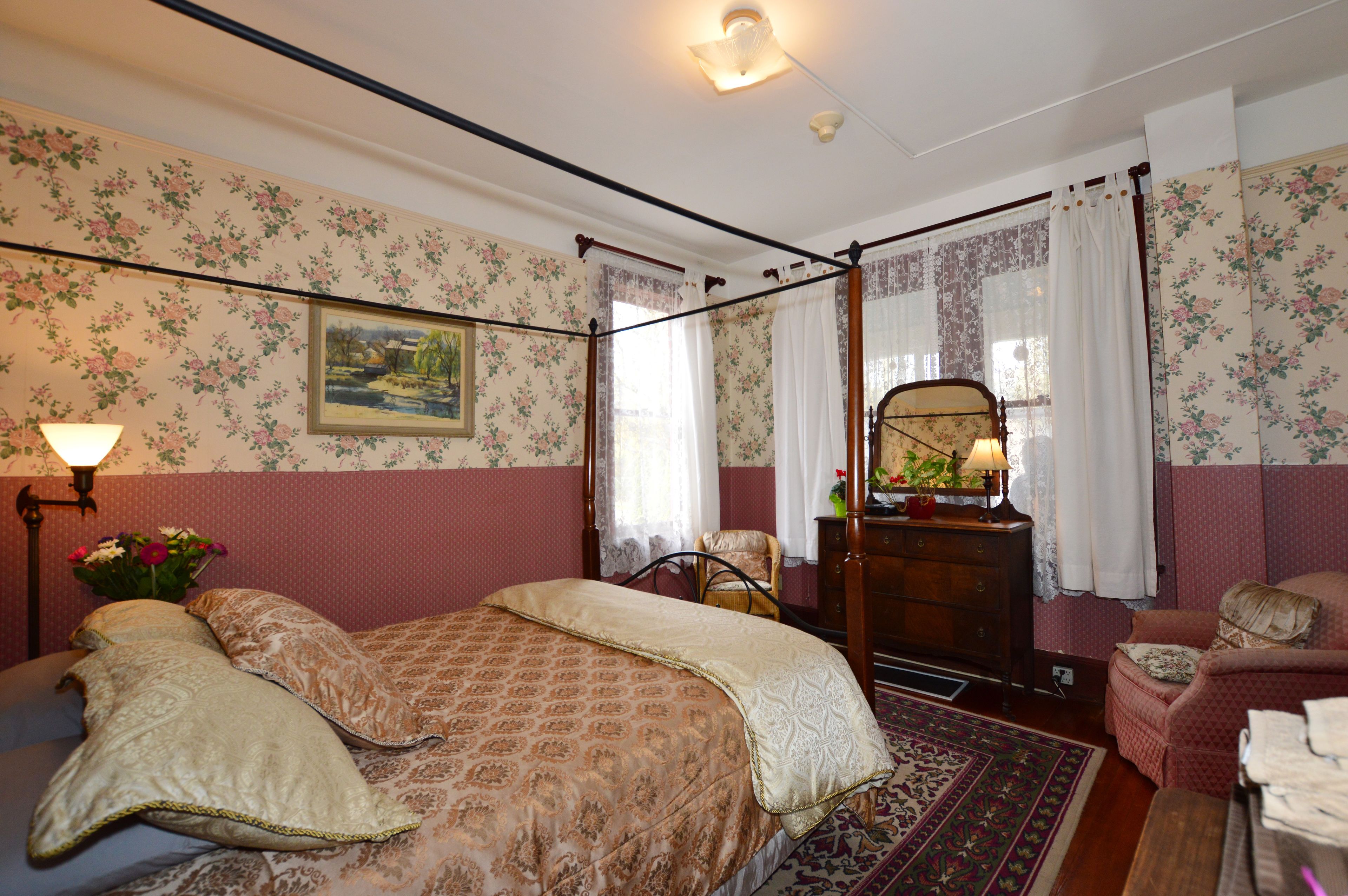 A bedroom with a four-poster bed, a dresser, a chair, and a small table.