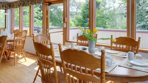 Comedor con mesas y sillas de madera, ventanas amplias con vistas a zonas verdes y un techo con estampado floral.