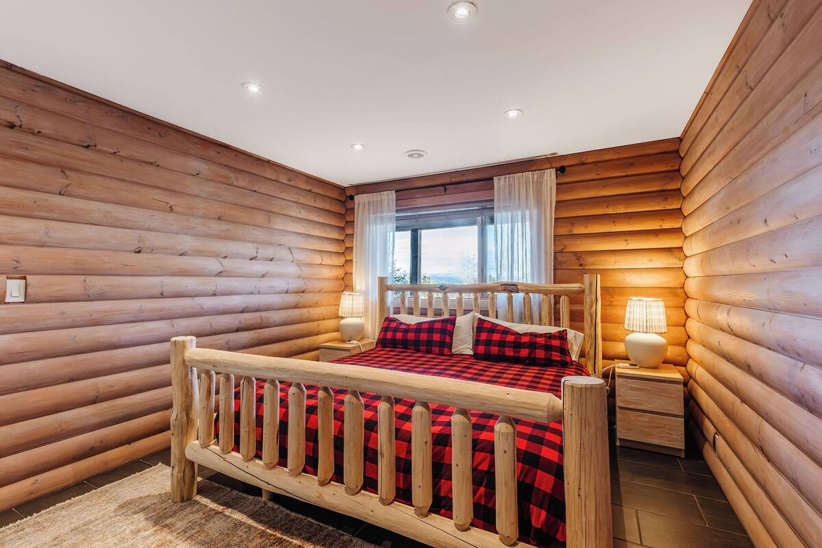 A wooden log cabin bedroom with a bed, two bedside tables, and a window with curtains.