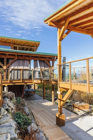 A wooden deck with a stone border, a covered outdoor seating area, and a view of a mountainous landscape.