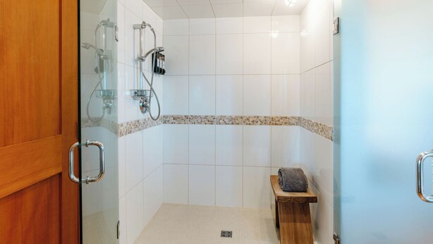 A glass-enclosed shower area with a tiled floor, a wooden bench, and a towel rack. - Myra Canyon Lodge + Ranch (Kelowna)