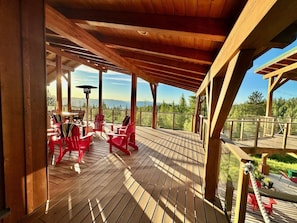 A wooden deck with red chairs and a table, overlooking a forested area.