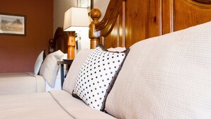 Une chambre d’hôtel avec une tête de lit en bois, un lit avec une literie blanche et des oreillers à pois, une table de chevet avec une lampe et un tableau encadré au mur.