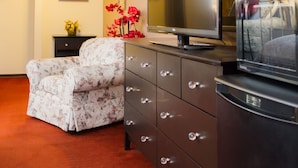 Une chambre d’hôtel équipée d’un téléviseur à écran plat, d’un fauteuil à motifs floraux, d’une commode et d’un miroir.