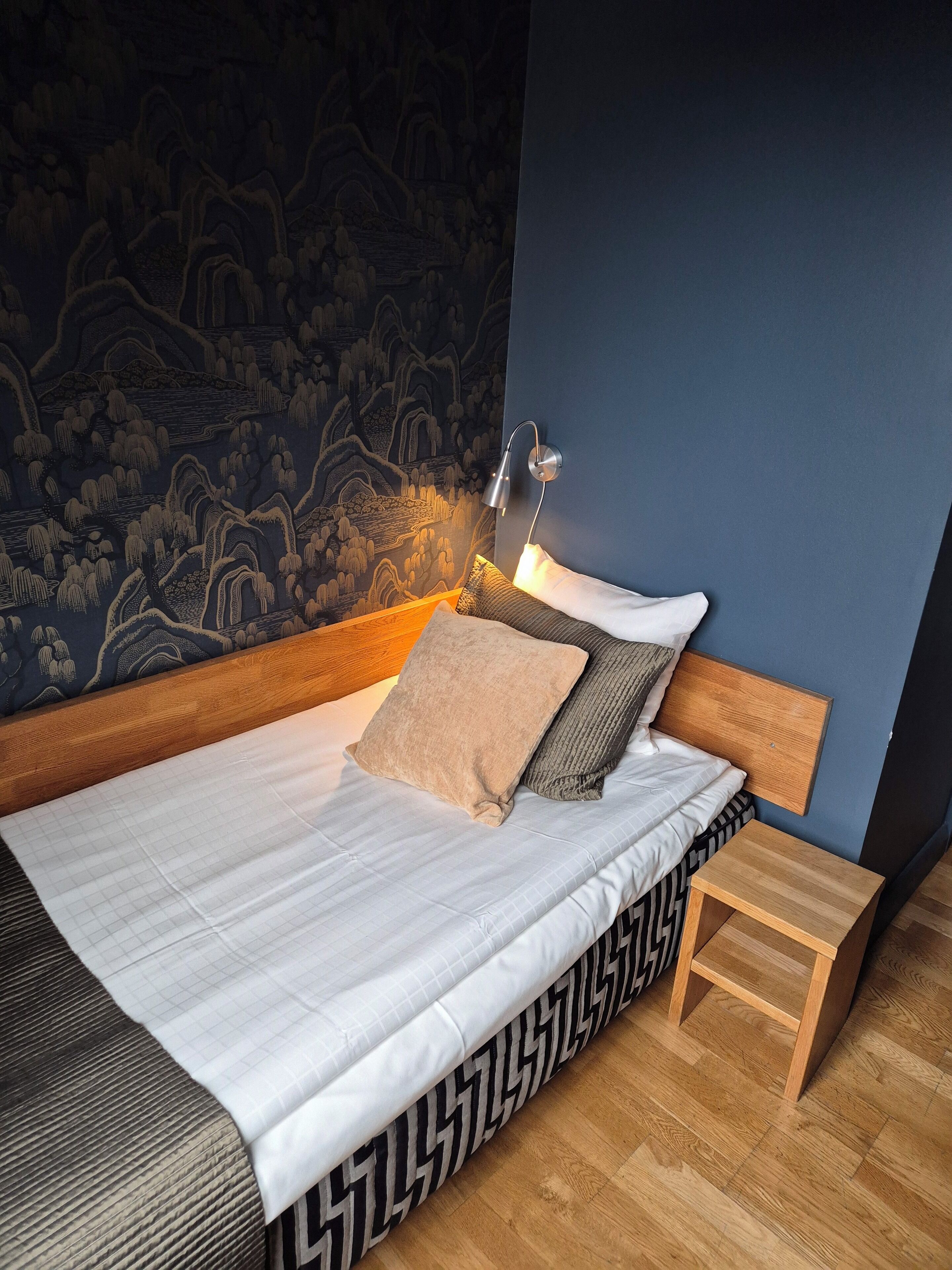A neatly made bed with a headboard, a bedside table, and a wall-mounted lamp.