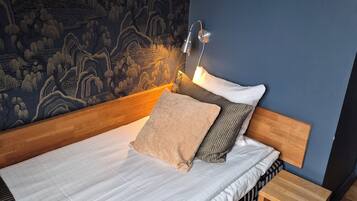 A neatly made bed with a headboard, a bedside table, and a wall-mounted lamp.