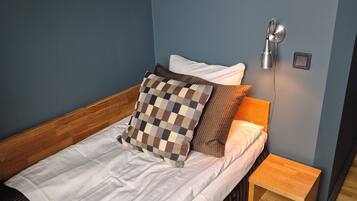 A neatly made bed with a checkered pillow, a bedside table, and a wall-mounted lamp.