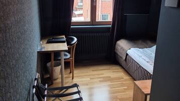 Una habitación pequeña con suelo de madera, una cama, un escritorio con silla y un radiador.