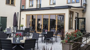 Un bâtiment doté d’un balcon, d’un espace repas avec des tables et des chaises, et d’un escalier menant à l’étage supérieur.