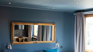 Un lit double avec une tête de lit en bois, deux tables de chevet, un miroir et une fenêtre avec des rideaux.