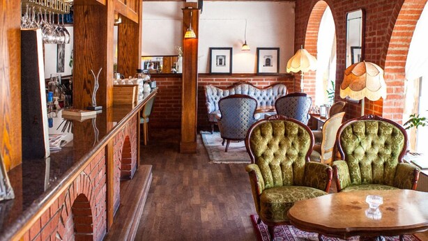 Un coin bar accueillant, avec des étagères en bois, un mur en briques et un espace salon comprenant des fauteuils rembourrés et une table ronde.