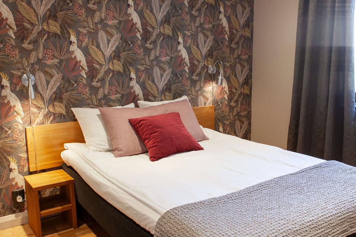 Een slaapkamer met een groot bed, houten nachtkastjes, behang met een patroon en uitzicht op de natuur.