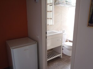 Un baño pequeño con lavamanos, inodoro y un refrigerador blanco compacto.