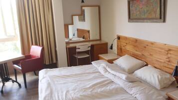 A hotel room with a bed, a desk, a chair, a mirror, and a painting on the wall.