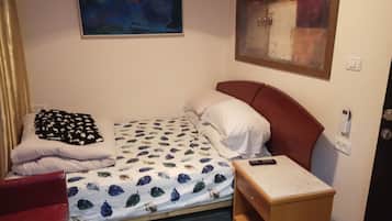 A small, neatly arranged bedroom with a bed, a bedside table, a red chair, and two paintings on the walls.