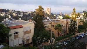 Un quartier résidentiel composé de plusieurs immeubles, dont certains sont dotés de panneaux solaires et d’antennes paraboliques, le tout entouré de verdure et offrant une vue lointaine sur la ville.