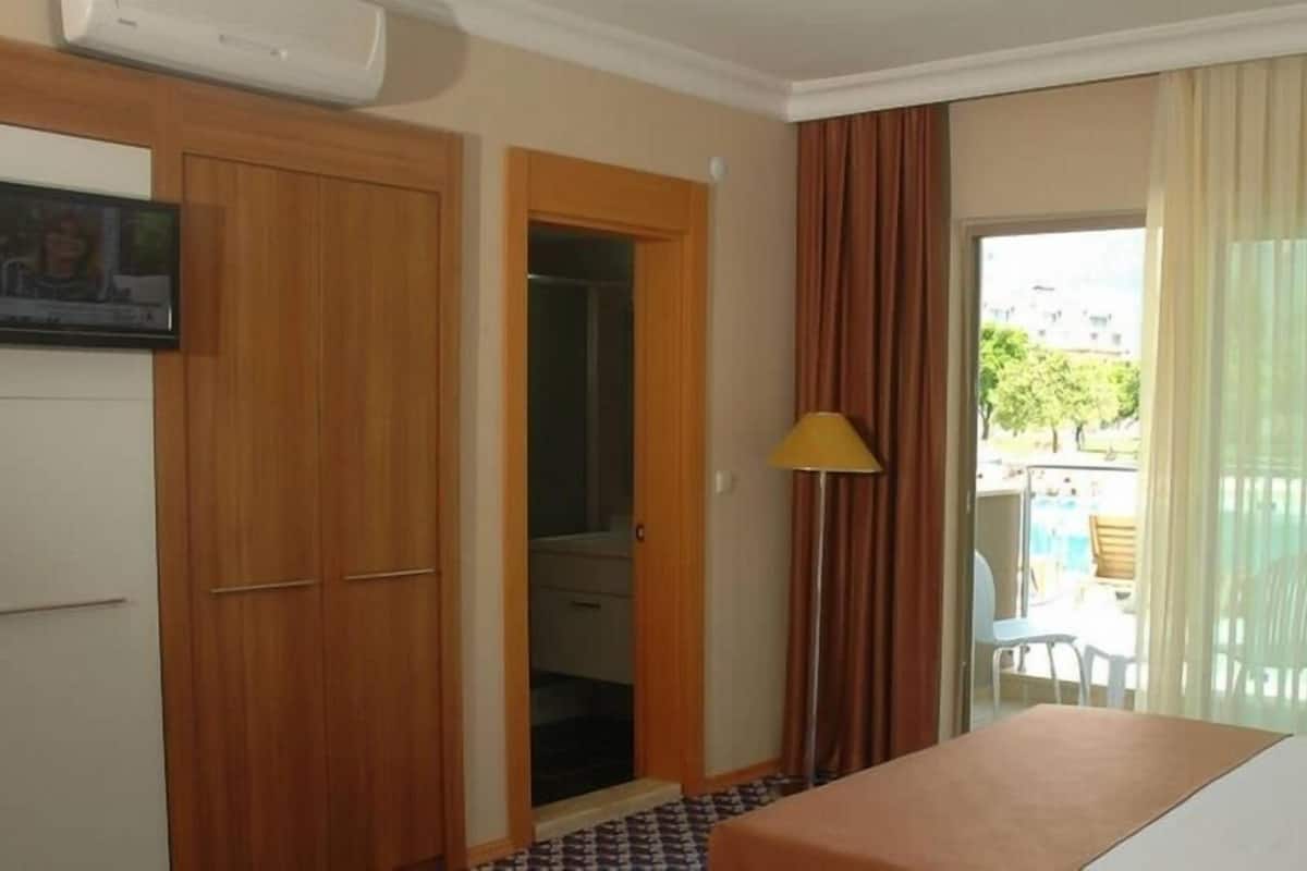 Habitación de hotel con cama, escritorio, televisión, armario y balcón con vistas al exterior.