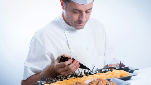 A chef in a white uniform pouring sauce over food.