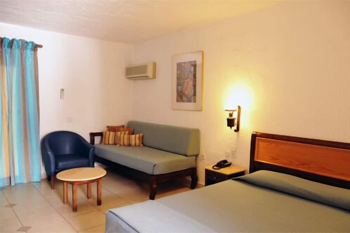 A hotel room with a bed, a sofa, a chair, a small table, and a nightstand.