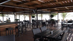 An outdoor dining area with wooden tables and chairs, a bar counter, and potted plants.
